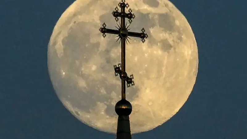 Bulan purnama di balik salib di atas sebuah gereja ortodoks di kota Rossosh di Voronezh, Rusia, pada Selasa 25 Mei 2021 (Kirill Kudryavtsev / AFP / Getty)