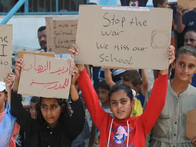 Sejumlah pelajar didampingi para aktivis Palestina mengangkat plakat saat berunjuk rasa menyerukan diakhirinya situasi perang di Gaza, di samping gedung sekolah yang rusak di Khan Yunis di Jalur Gaza selatan pada 28 Agustus 2024. (Bashar TALEB/AFP)