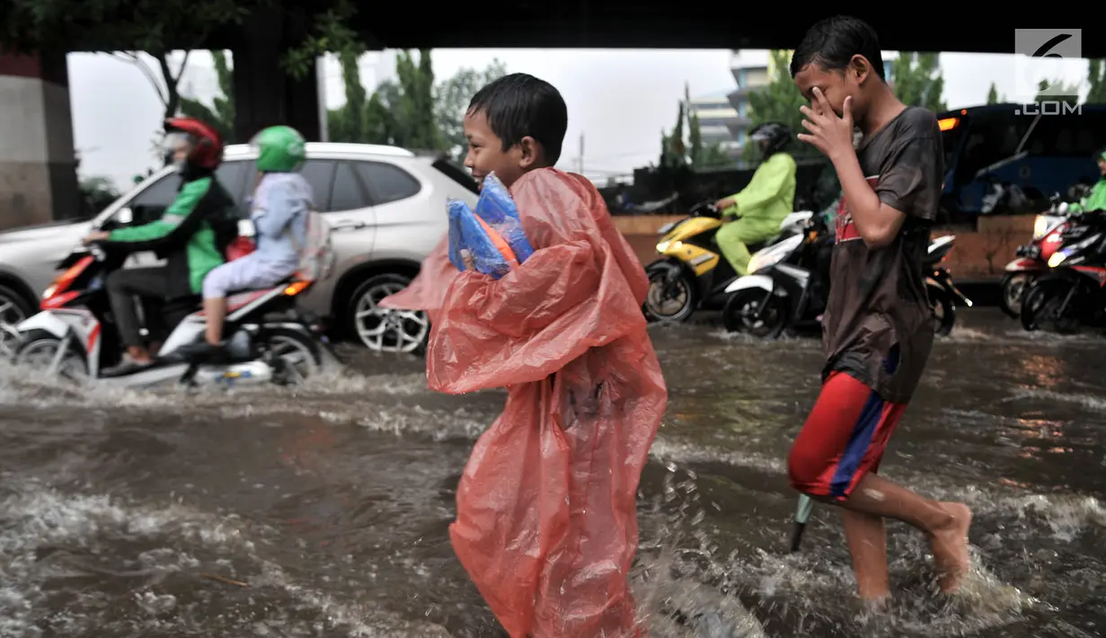 Anak-anak penjual jas hujan dan ojek payung bermain air saat banjir menggenangi Jalan DI Panjaitan, Jakarta, Senin (3/12).  Menurut petugas, banjir disebabkan oleh buruknya sistem drainase atau gorong-gorong. (Merdeka.com/ Iqbal S. Nugroho)