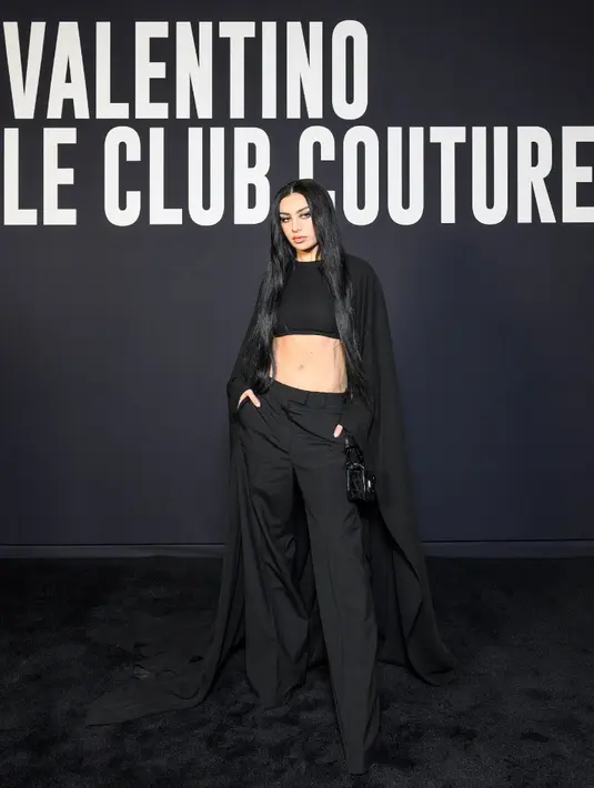 Charli XCX tampil serba hitam dengan crop top, long outer, dan celananya. Outfit tersebut merupakan koleksi  Spring Summer 2023 Unboxing. Credit: Valentino/SGP Italia