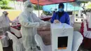 Petugas Kelompok Penyelenggara Pemungutan Suara (KPPS) dengan memakai baju hazmat membantu pemilih memasukkan kertas suara usai menggunakan hak pilihnya dalam Pilkada Tangerang Selatan 2020 di TPS 46, Paku Jaya, Serpong Utara, Rabu (9/12/2020). (merdeka.com/Arie Basuki)