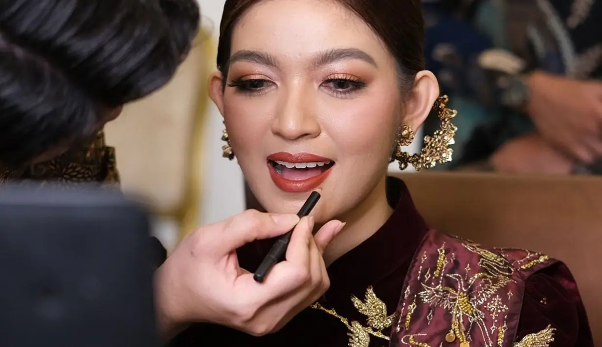 Selvi Ananda dimakeup bold dengan area mata yang lebih playful; menggunakan warna merah serasi dengan pulasan lipstiknya, smokey eyes tipis, rambut yang ditata sleek dengan aksesori keemasan yang pas secara keseluruhan. [Foto: Instagram/rama_jee]