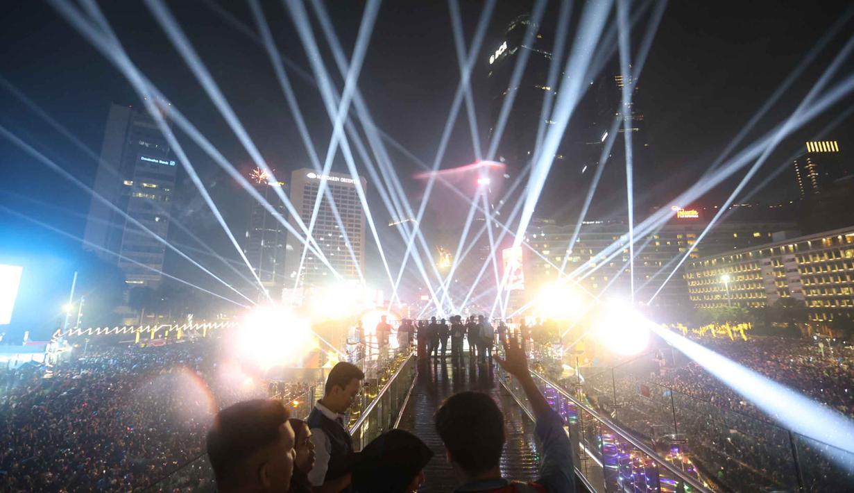 Atraksi drone dan cahaya lampu ini menjadi salah satu hiburan visual utama dalam rangkaian perayaan Tahun Baru 2026 yang digelar Pemprov DKI Jakarta. Tampak dalam foto, warga berfoto dengan latar cahaya lampu saat perayaan malam pergantian tahun di kawasan Bundaran Hotel Indonesia, Jakarta, Rabu (31/12/2025). (Kapanlagi.com/Budy Santoso)