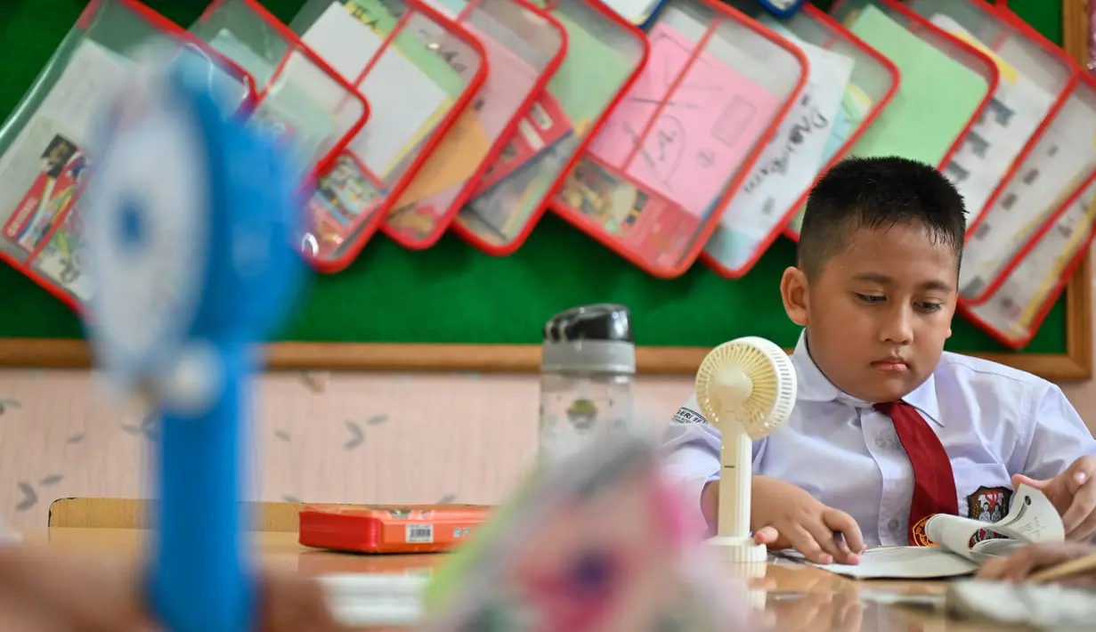 Seorang siswa sekolah dasar menggunakan kipas angin portabel untuk menyejukkan ruangan kelas saat cuaca panas di Banda Aceh pada 15 Mei 2023. (AFP/CHAIDEER MAHYUDDIN)