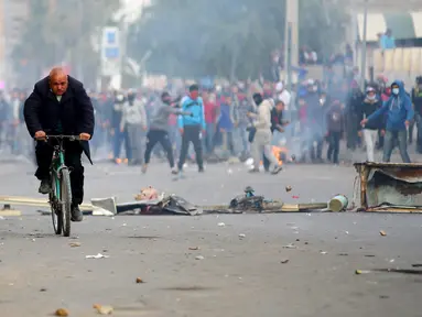 Seorang pria mengendarai sepeda saat pengunjuk rasa melemparkan batu ke arah polisi di luar kantor pemerintah setempat di Kasserine, Tunisia, Kamis (21/1). Mereka menuntut solusi dari masalah pengangguran yang meliputi negaranya. (REUTERS/Amine Ben Aziza)