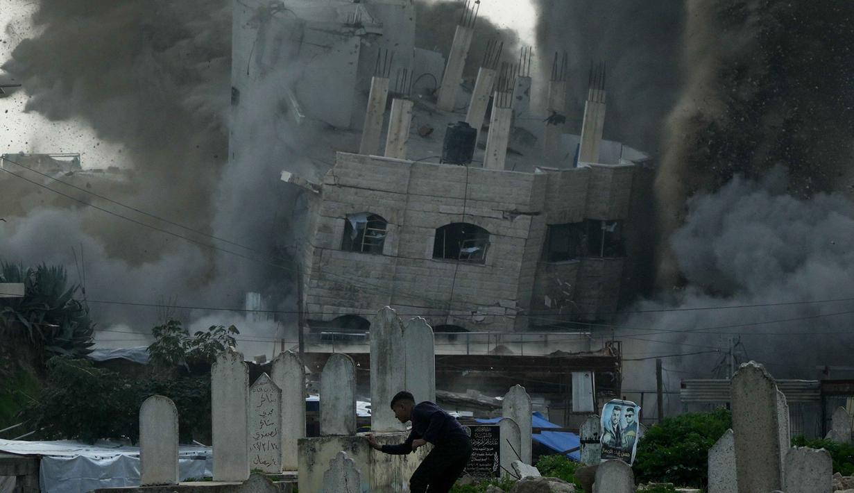 Serangan terjadi di tengah meningkatnya ketegangan dan tuduhan pelanggaran kesepakatan gencatan senjata yang masih berlaku. Tampak dalam foto, seorang pria berlari mencari perlindungan di pemakaman saat asap mengepul dari serangan militer Israel terhadap sebuah bangunan di lingkungan Zeitoun, Kota Gaza, Jumat 6 Februari 2026. (AP Photo/Jehad Alshrafi)