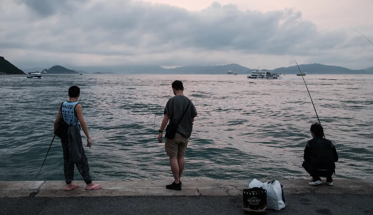 Sejumlah pria memancing dari dermaga di Victoria Harbour di Hong Kong (21/4/2020). Kepala eksekutif Carrie Lam mengatakan langkah-langkah jarak sosial dan beberapa pembatasan bisnis akan berlanjut selama dua minggu hingga setidaknya 7 Mei. (AFP/Anthony Wallace)