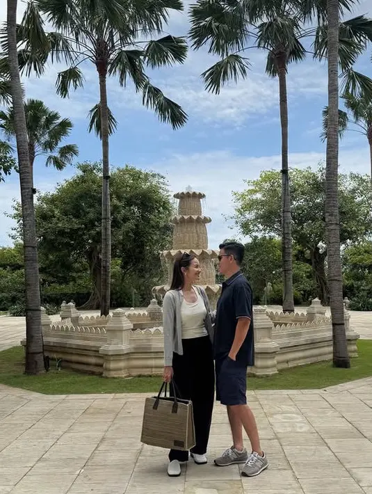Enzy Storia liburan lebaran bersama suaminya ke Bali. Tampak ia mengenakan outer cardigan abu-abu dipadukan inner tanktop putih serta celana panjang hitam. Membawa tas tote bag besar, serta flat shoes putih. [@enzystoria]