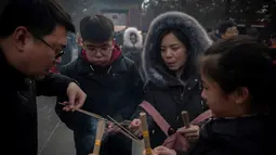 Keluarga membakar dupa untuk berdoa keberuntungan pada hari kelima Tahun Baru Imlek di Yonghegong, atau Kuil Lama di Beijing (9/2). Warga China merayakan Tahun Babi tersebut dengan doa, pesta keluarga, dan belanja. (AFP Photo/Nicolas Asfouri)