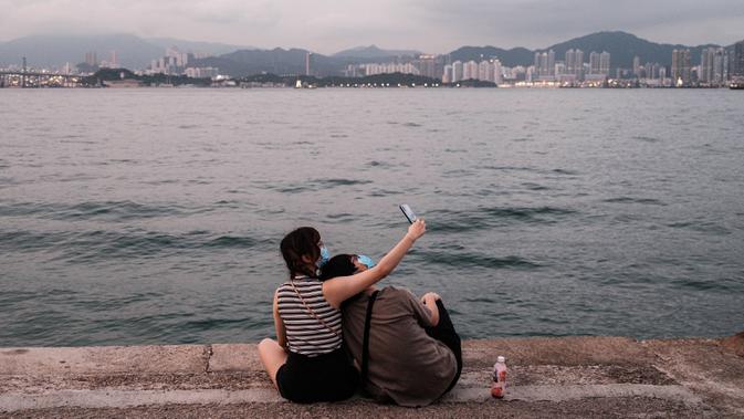 Pasangan berselfie di dermaga kargo yang dijuluki 'Dermaga Instagram' di Hong Kong (21/4/2020). Hong Kong melaporkan penurunan kasus infeksi harian Covid-19, tetapi pemerintah kota mengatakan mereka tidak mengambil risiko apa pun. (AFP/Anthony Wallace)