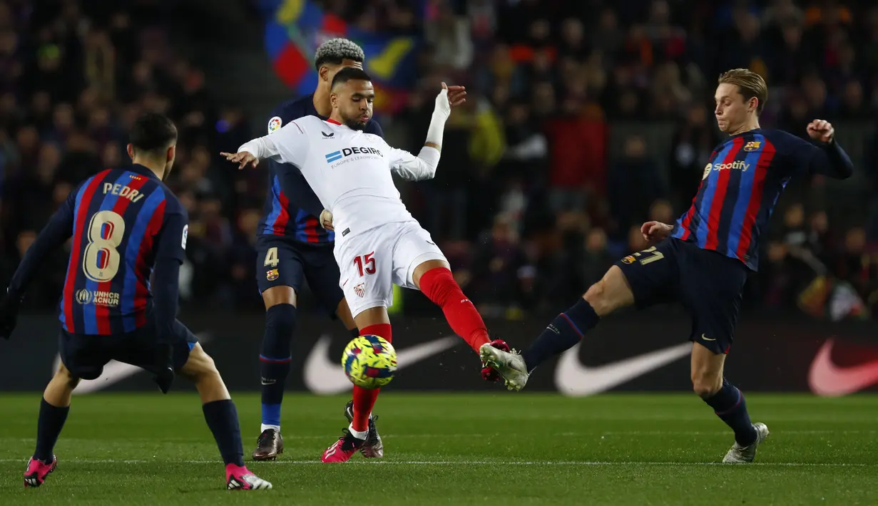 Penyerang Sevilla Youssef En-Nesyri berebut bola dengan Barcelona Frenkie de Jong, Pedri, dan Ronald Araujo pada jornada ke-20 La Liga 2022/2023 di Camp Nou, Senin (6/2/2023) dini hari. Kini Barca memimpin dengan 53 poin dari 20 pertandingan. (AP Photo/Joan Monfort)