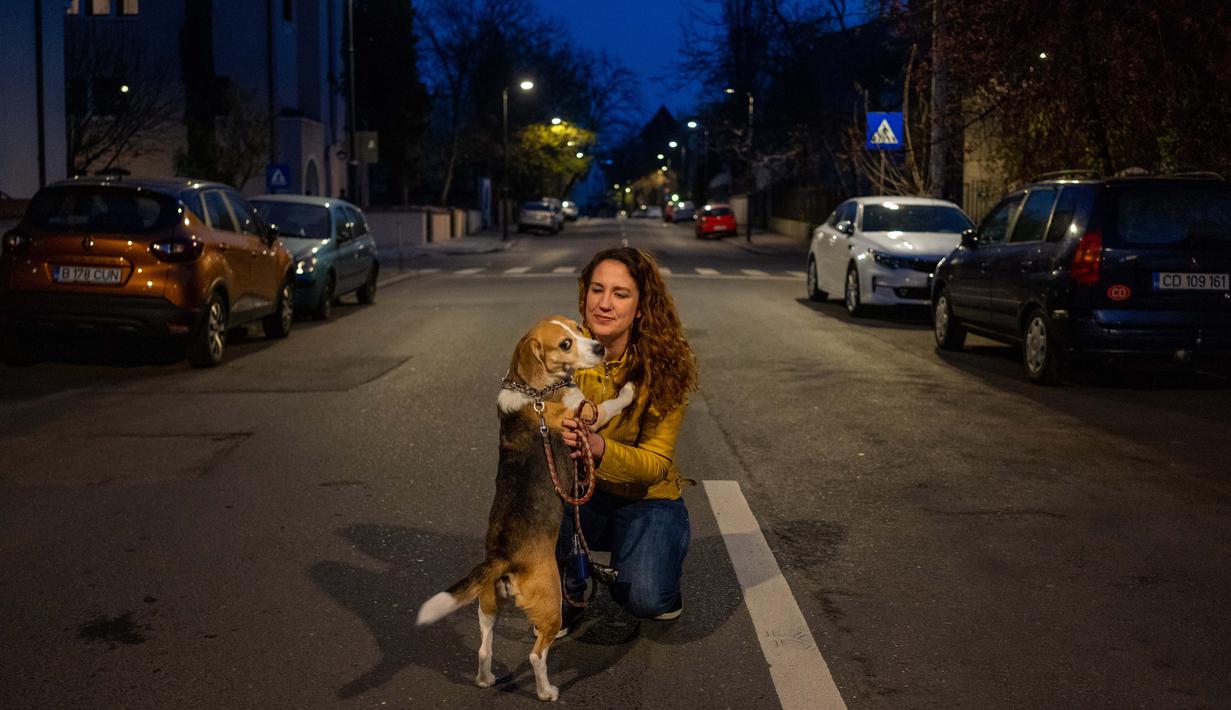 Catalina Gherghel (34) berpose dengan anjingnya Ziggy Stardust  (7) di Bucharest (29/3/2020). Undang-undang militer, yang disahkan pemerintah Rumania untuk mengurangi penyebaran virus corona, menyatakan berjalan bersama anjing adalah salah satu  kegiatan yang masih diizinkan. (AFP/Andrei Pungovschi)