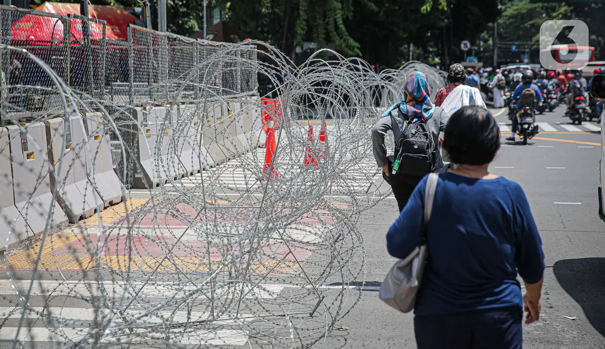 Warga berjalan dekat kawat berduri di kawasan Jalan MH Thamrin, Jakarta, Kamis (2/12/2021). Polda Metro Jaya memasang barikade di sejumlah titik menuju kawasan Patung Kuda-Monumen Nasional (Monas) Jakarta Pusat guna mengantisipasi kerumunan massa aksi Reuni 212. (Liputan6.com/Faizal Fanani)