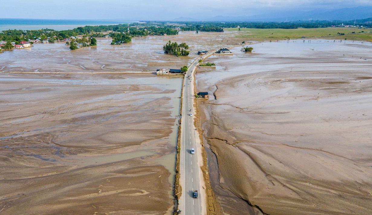 Data sementara posko tanggap darurat bencana Aceh per 7 Desember 2025, kerusakan lahan pertanian di provinsi itu akibat bencana hidrometeorologi sejak 25 November lalu telah mencapai lebih dari 65 ribu hektare. Tampak foto udara menunjukkan warga berkendara melewati sawah yang terendam lumpur setelah banjir bandang di Meureudu, Kabupaten Pidie Jaya, Provinsi Aceh, pada Senin 8 Desember 2025. (Chaideer MAHYUDDIN/AFP)