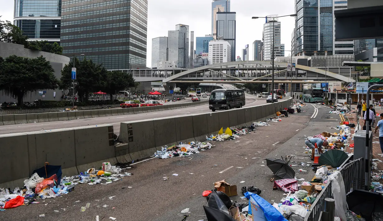 Orang-orang berjalan di jalan yang penuh sampah sehari setelah demonstrasi menolak RUU ekstradisi di Hong Kong (13/6/2019). Aksi tersebut berujung bentrok antara polisi dan warga dimana puluhan ribu orang memblokir jalan-jalan di kota tersebut. (AFP Photo/Anthony Wallace)