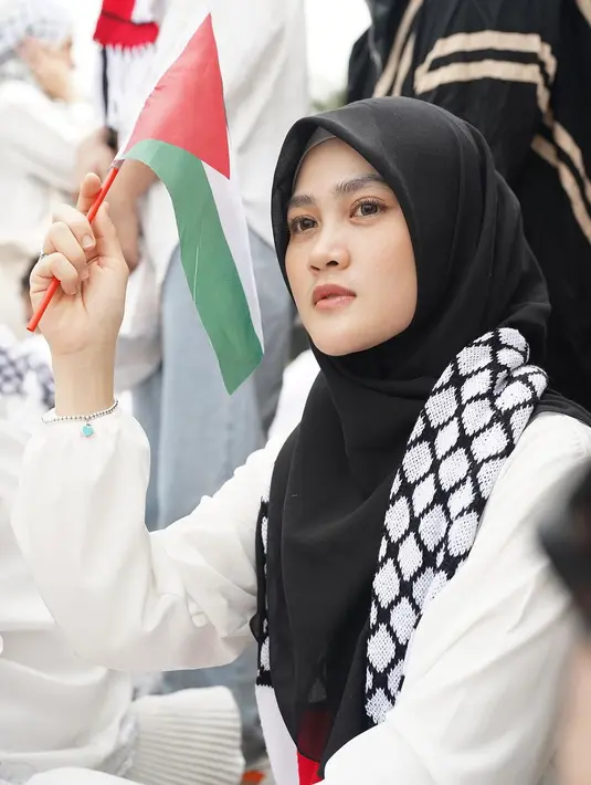 Hadiri aksi bela Palestina, Henny Rahman datang bersama Alvin Faiz. Henny Rahman tampil sederhana dengan jilbab hitam, syal Palestina dan makeup yang sangat natural. Artis berusia 29 tahun ini tak lupa memakai atribut dan bawa bendera Palestina. Dalam keterangan unggahannya, Henny berharap aksi tersebut bisa membuka mata dunia dan berharap Palestina segera merdeka. (Liputan6.com/IG/@alvin_411)