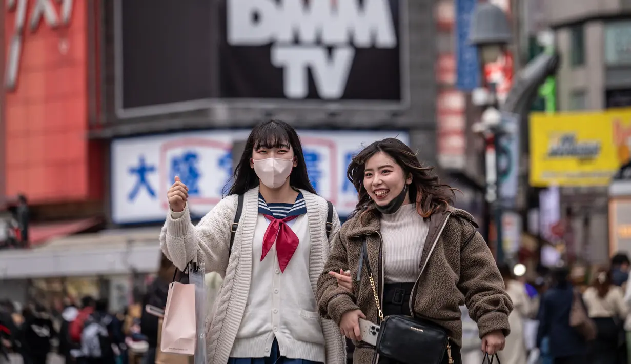 Dua perempuan menyeberang jalan di distrik Shibuya Tokyo pada hari pertama pemerintah Jepang mencabut ketentuan wajib mengenakan masker, Senin (13/3/2023).Meski kewajiban masker berakhir, tak mudah mengubah perilaku masyarakat yang sudah terbiasa menggunakan penutup wajah ini. (Photo by Yuichi YAMAZAKI / AFP)