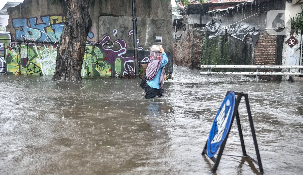 Warga melintasi banjir yang merendam Jalan Abdullah Syafei, Tebet, Jakarta, Kamis (18/2/2021). Hujan deras yang mengguyur sejak pagi tadi menyebabkan aliran Kali Tebet meluap hingga merendam Jalan Abdullah Syafei dengan ketinggian mencapai sepaha orang dewasa. (merdeka.com/Iqbal S Nugroho)