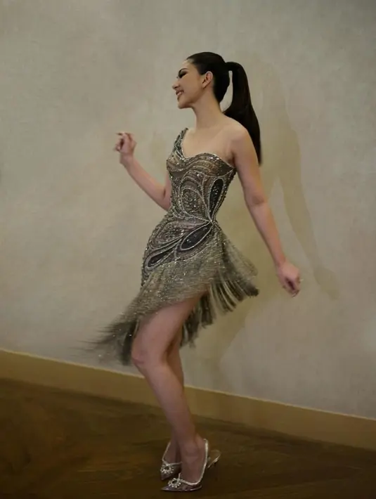 Strapless dress itu hadir dengan ilusi neckline, dihiasi detail manik-manik berkilauan serta pinggiran asimetris menambah kemewahan.