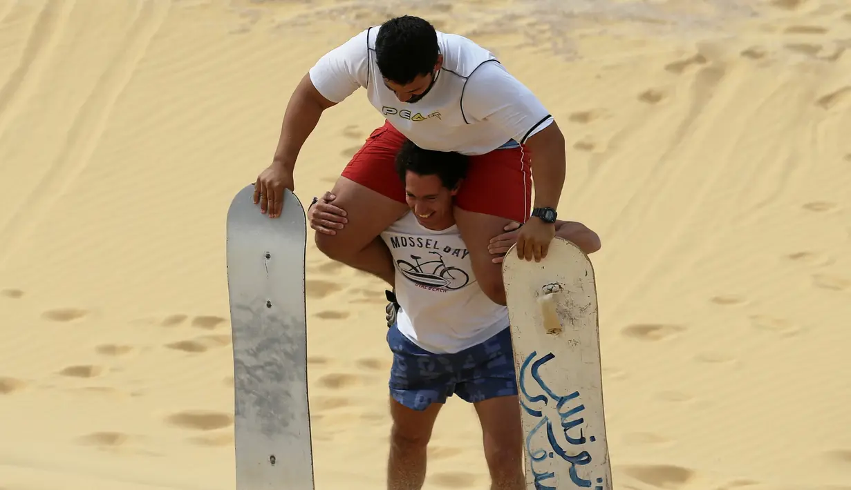 Pengunjung menggendong temannya setelah berseluncur di gurun pasir Wadi el-Rayan Fayoum, Mesir (18/11). Di gurun ini menyajikan banyak hiburan dan pariwisata salah satunya, berseluncur di pasir atau sandboarding. (Reuters/Mohamed Abd El Ghany)