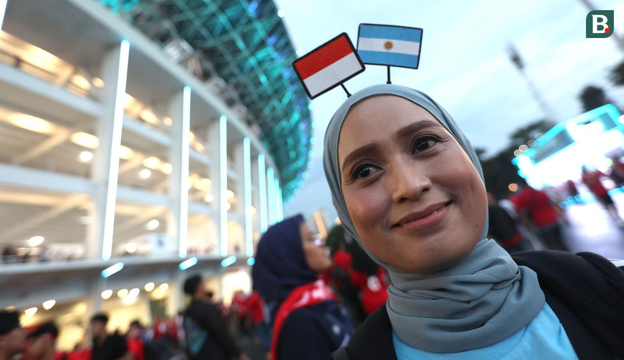 Seorang suporter wanita mengenakan bando bendera Indonesia dan Argentina berpose di depan fotografer sebelum laga FIFA Matchday antara Timnas Indonesia melawan Argentina di Satdion Utama Gelora Bung Karno (SUGBK), Senayan, Jakarta, Senin (19/06/2023). (Bola.com/Bagaskara Lazuardi)