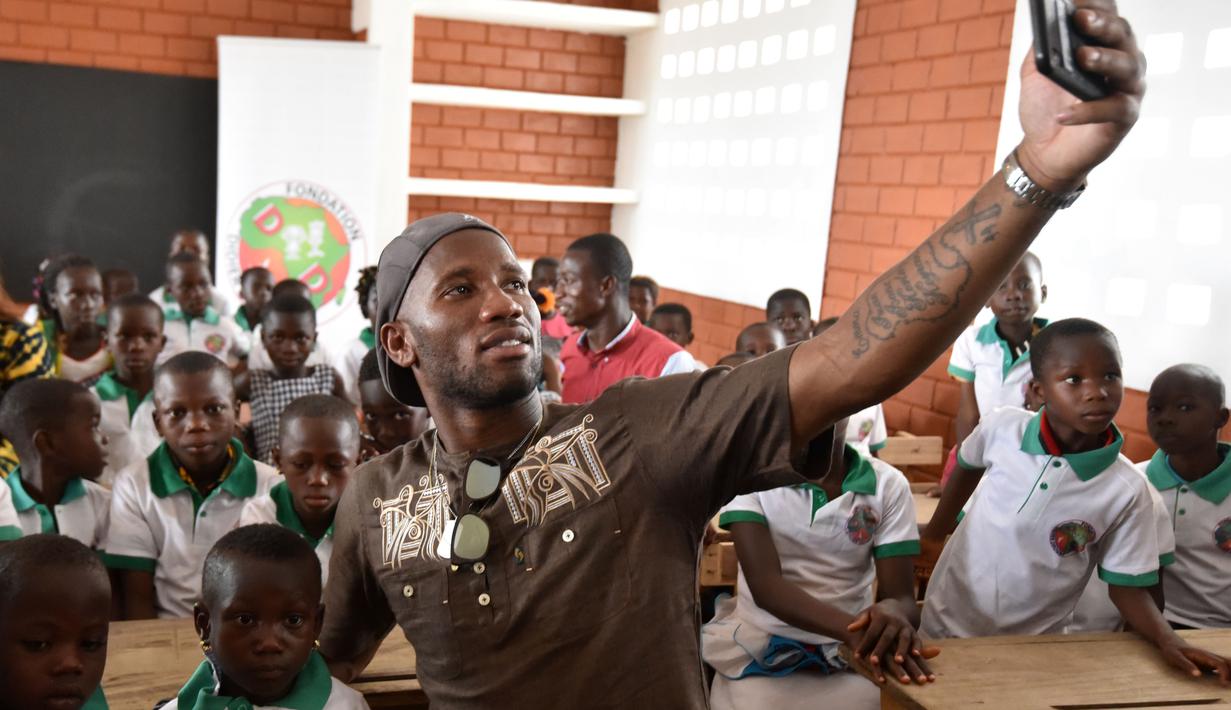 Didier Drogba melakukan foto selfie bersama anak-anak saat membuka sekolah dasar di Onahio, Pokou-Kouamekro, Pantai Gading, (20/1/2018).  Drogba menjadi salah satu sponsor utama untuk sekolah tersebut. (AFP/Sia Kambou)