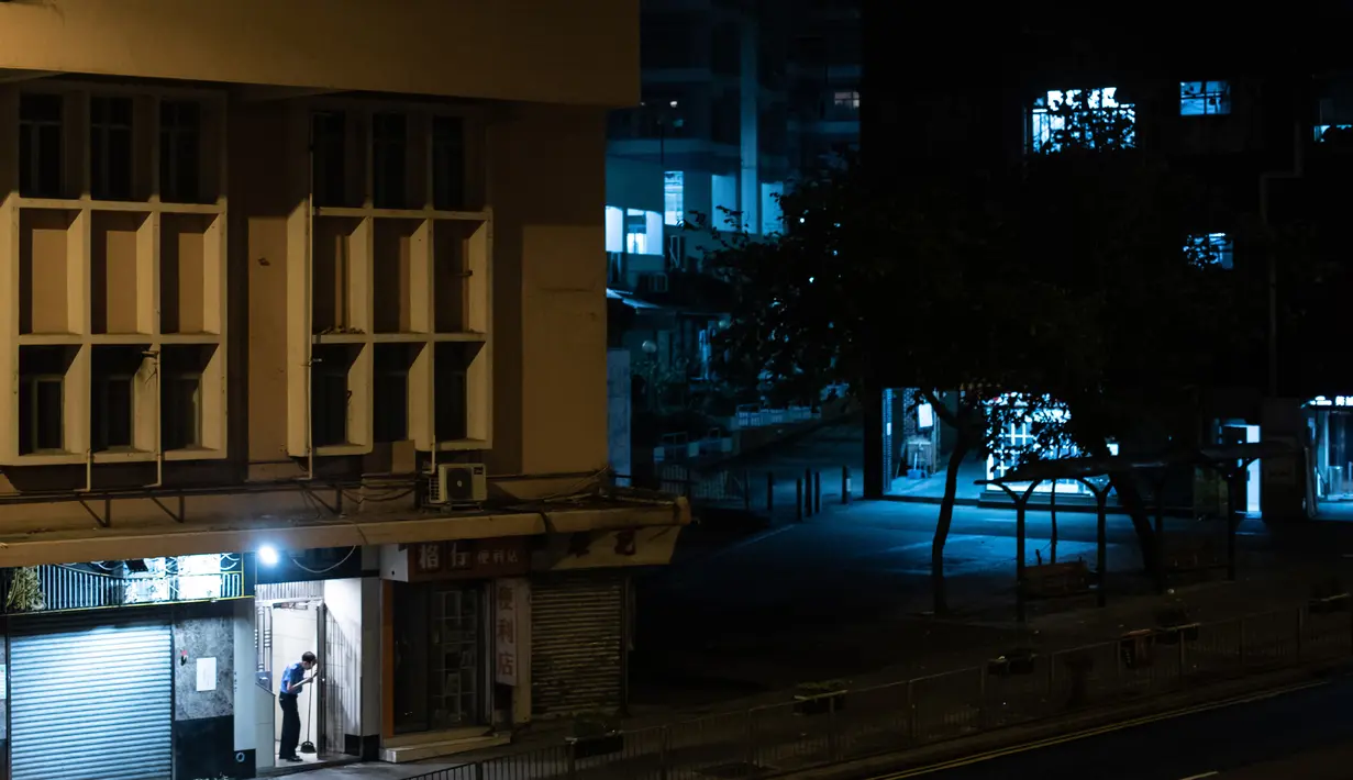 Penjaga keamanan memegang sapu pada subuh hari di pintu masuk sebuah bangunan di distrik Kwai Chung, Hong Kong (25/5/2019). Kwai Chung adalah situs pelabuhan peti kemas. Ini juga merupakan bagian dari Kota Baru Tsuen Wan. Pada tahun 2000, ia memiliki populasi 287.000. (AFP Photo/Philip Fong)