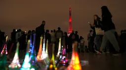 Wisatawan berjalan melewati replika Menara Eiffel yang dijual saat pertunjukan instalasi cahaya di Paris, Perancis, Kamis (13/9). Pertunjukan ini bagian dari kunjungan Putra Mahkota Jepang, Naruhito. (AP Photo/Christophe Ena)