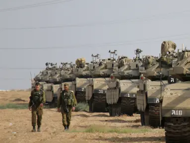 Tentara Israel berjalan melewati tank di dekat perbatasan Gaza-Israel, Jumat (19/10). Sekitar 60 tank dan kendaraan lapis baja pengangkut personel bergerak melalui jalan-jalan Israel menuju perbatasan Gaza. (AP Photo/Ariel Schalit)