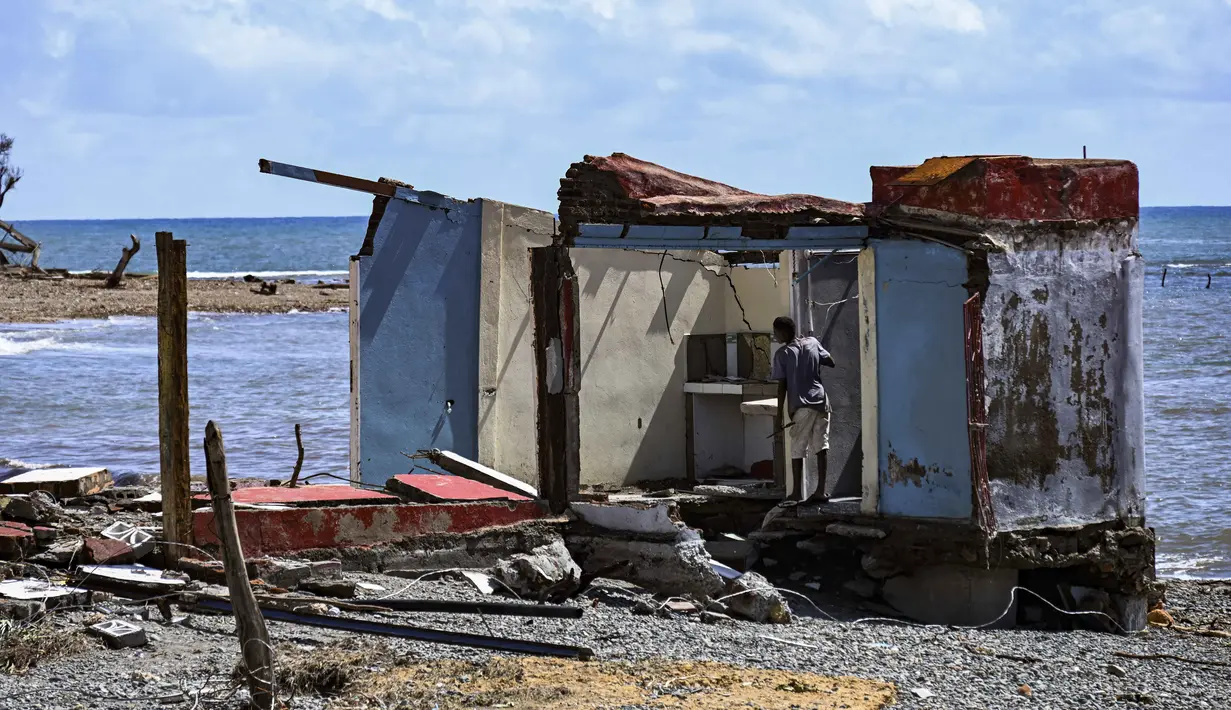 Seorang pria berdiri di samping sebuah rumah yang rusak akibat Badai Melissa di desa Boca de Dos Rios, provinsi Santiago de Cuba, Kuba pada Kamis 30 Oktober 2025. Sementara, kerusakan terparah dilaporkan terkonsentrasi di wilayah barat daya dan barat laut. (YAMIL LAGE/AFP)