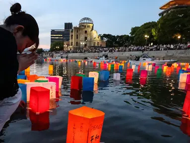 Foto yang diambil pada tanggal 6 Agustus 2024 ini menunjukkan seorang wanita yang sedang berdoa saat lentera dilepaskan ke Sungai Motoyasu, di seberang Kubah Bom Atom dekat Taman Peringatan Perdamaian di Hiroshima. (JIJI Press/AFP/Japan OUT)