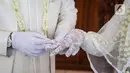 Pengantin pria memasangkan cincin ke pasangannya usai akad nikah di KUA Jagakarsa, Jakarta, Sabtu (6/6/2020). Pada masa penerapan PSBB transisi, pihak KUA tersebut menikahkan sebanyak delapan hingga 10 pasangan pengantin per hari. (Liputan6.com/Faizal Fanani)