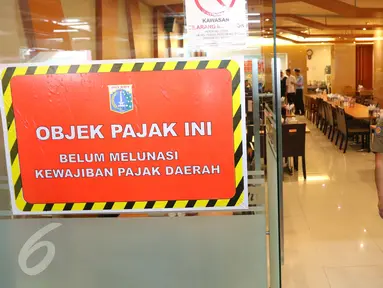Petugas berjalan di samping stiker penunggak pajak yang dipasang di sebuah restoran di pusat perbelanjaan di kawasan Senayan, Jakarta, Senin (5/9). Pemasangan stiker dilakukan Dinas Pelayanan Pajak DKI lantaran menunggak pajak. (Liputan6.com/Angga Yuniar)