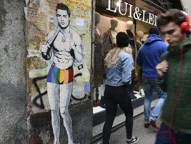 Sejumlah warga melintasi mural dengan gambar bintang Juventus, Cristiano Ronaldo, yang terdapat di Milan, Senin (19/3). Mural berjudul Cristiano's Secret ini karya seniman Italia, TvBoy. (AFP/Miguel Medina)