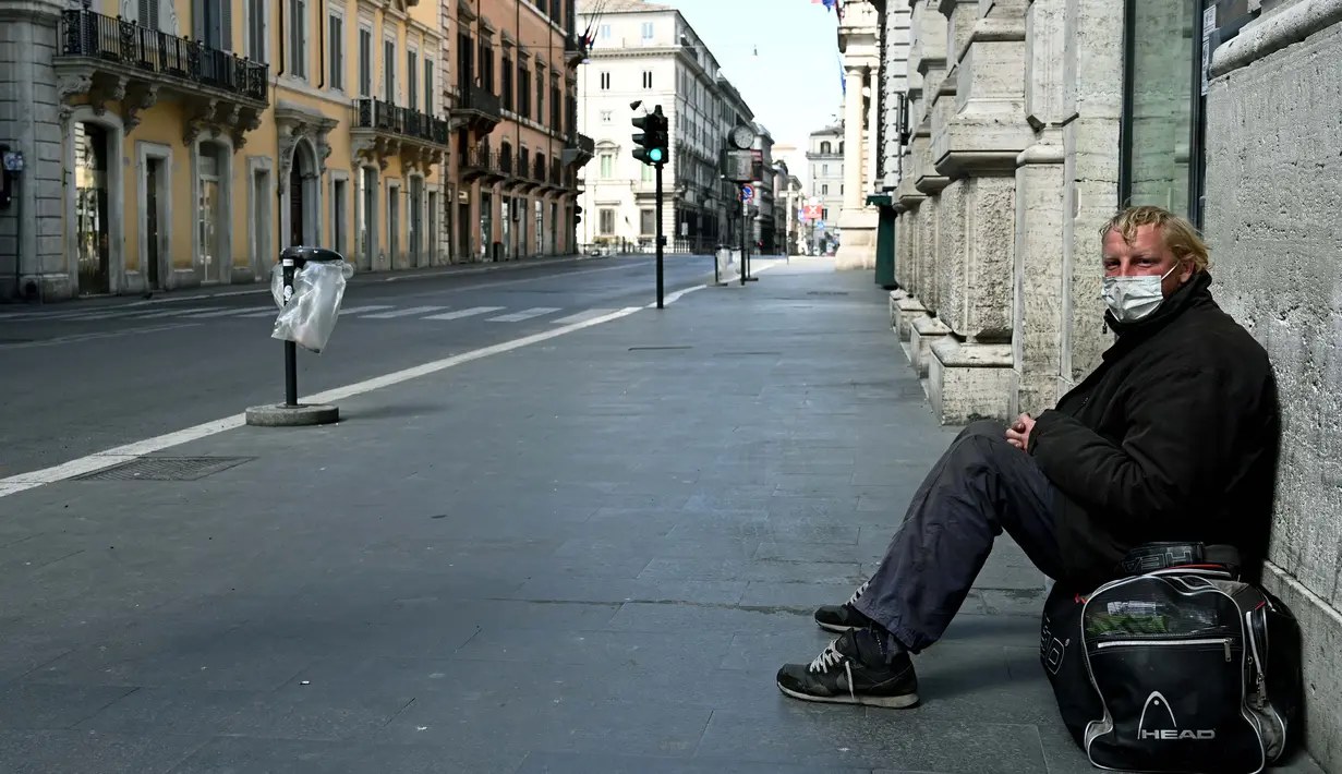 Seorang tunawisma duduk di jalan utama Via del Corso yang sepi setelah pemerintah Italia melakukan lockdown untuk menghentikan penyebaran pandemi COVID-19 di Roma pada 24 Maret 2020. (Photo by Vincenzo PINTO / AFP)