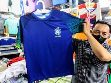 Seorang pria menunjukkan jersey timnas sepak bola peserta Piala Dunia Qatar 2022 di salah satu kios Blok B Pasar Tanah Abang, Jakarta, Kamis (24/11/2022). Menurut pedagang, permintaan jersey timnas meningkat dikarenakan Piala Dunia Qatar 2022 yang dimulai sejak 20 November 2022. (Liputan6.com/Johan Tallo)