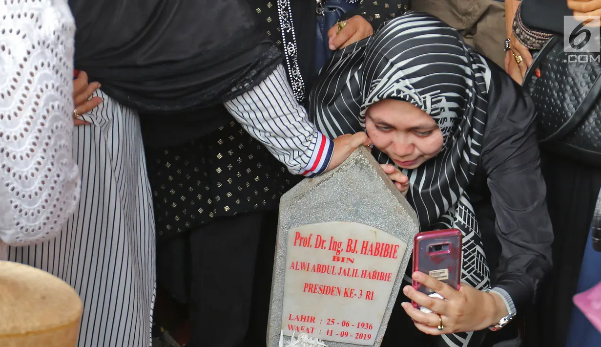 Seorang wanita berswafoto dengan batu nisan Presiden ketiga BJ Habibie di Taman Makam Pahlawan Nasional Kalibata, Jakarta, Kamis (12/9/2019). Selain berdoa, tidak sedikit juga warga  mengabadikan dengan kamera ponsel. (Liputan6.com/Herman Zakharia)