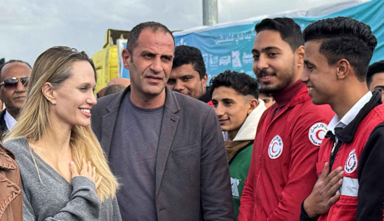 Diketahui, saat ini, Gaza sedang menghadapi musim dingin yang ekstrem, dengan hujan lebat dan penurunan suhu yang memperburuk kondisi para pengungsi. Tampak dalam foto, aktris Amerika Serikat (AS), Angelina Jolie (kiri) menyapa seorang karyawan Bulan Sabit Merah Mesir di perbatasan Rafah Mesir, pada Jumat 2 Januari 2026. (Foto oleh AFP)