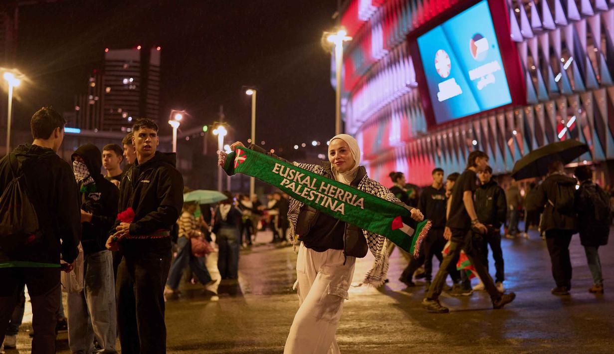 Ribuan orang turun ke jalan sebelum pertandingan dimulai, berbaris sambil mengibarkan bendera dan menyerukan dukungan untuk Gaza. Tampak dalam foto, seorang wanita memegang syal bermotif simbol Palestina menjelang pertandingan persahabatan antara tim pemain Palestina dan sekelompok pemain Spanyol dari wilayah Basque, yang diadakan sebagai protes terhadap aksi militer Israel di Gaza, di Bilbao, Spanyol, Sabtu 15 November 2025. (AP Photo/Miguel Oses)