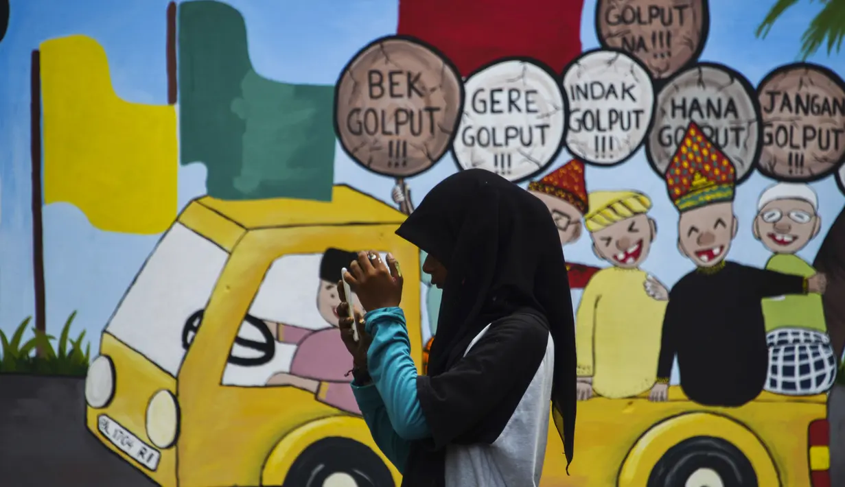 Seorang wanita melintas di depan mural Pemilu 2019 di Banda Aceh, provinsi Aceh (17/3). Indonesia akan mengadakan pemilihan presiden dan parlemen secara serentak pada 17 April. (AFP Photo/Chaideer Mahyuddin)