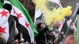 Pemberontak yang dipimpin oleh kelompok Islamis menggulingkan penguasa lama Suriah, Bashar al-Assad. Tampak dalam foto, anggota komunitas Suriah melambaikan bendera Suriah dan menyalakan suar pada tanggal 8 Desember 2024 di Berlin, Jerman, untuk merayakan berakhirnya kekuasaan rezim Bashar al-Assad. (RALF HIRSCHBERGER/AFP)