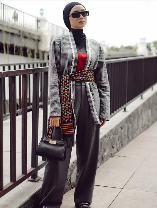 Tampil dengan wastra mengenakan kebaya loose abu-abu garis list renda, dipadukan inner turtleneck hitam senada dengan turabannya. Dipadukan belt kain bermotif serta celana panjang abu-abu. [@ansellmaputri]
