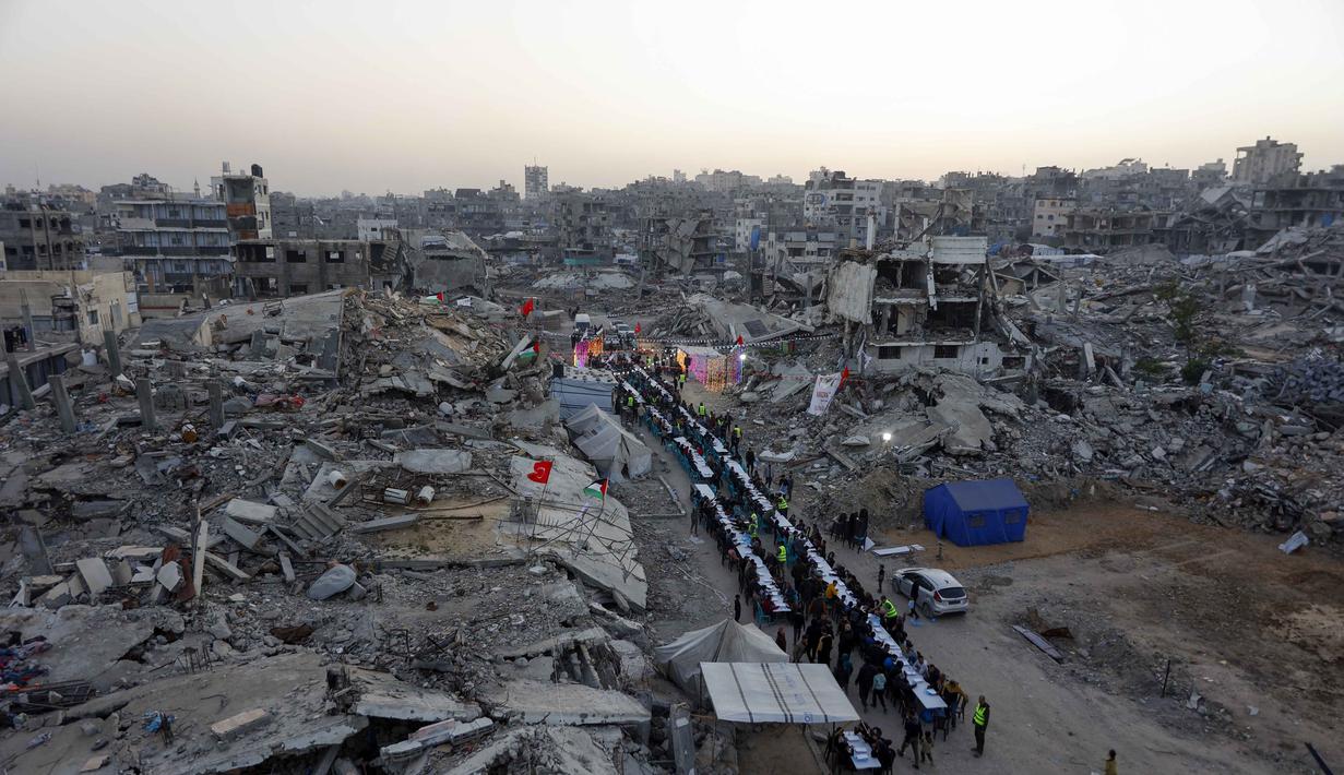 Yayasan IHH Turki berfokus menyalurkan bantuan kemanusiaan kepada korban perang, bencana alam, kemiskinan, serta melakukan pembangunan infrastruktur seperti sekolah, masjid, dan fasilitas kesehatan. Tampak dalam foto, warga Palestina berkumpul untuk berbuka puasa bersama yang diselenggarakan oleh Yayasan IHH Turki, di tengah reruntuhan bangunan yang hancur di Kota Gaza pada Rabu 18 Februari 2026. (Omar AL-QATTAA/AFP)