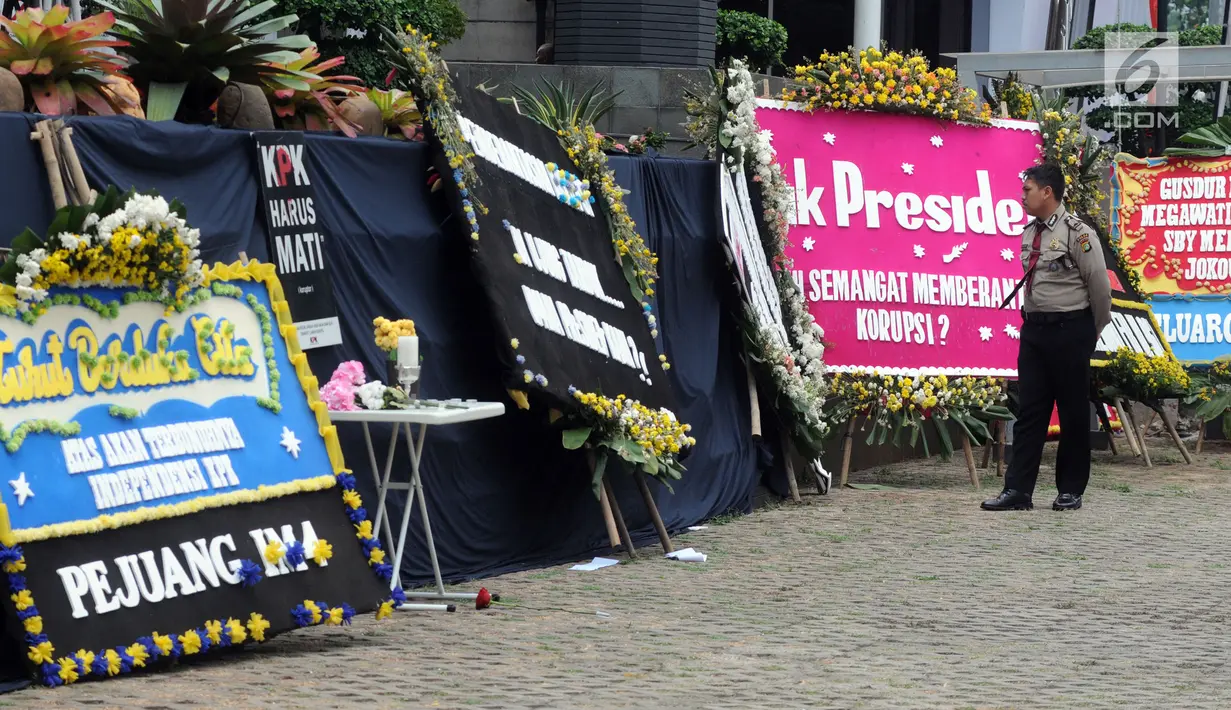 Petugas kepolisian mengamati karangan bunga ucapan belasungkawa atas kematian KPK di Gedung Merah Putih, Jakarta, Senin (9/9/2019). Keberadaan kain hitam dan karangan bunga ini merupakan bentuk protes atas revisi Undang-undang KPK yang dinilai dapat melemahkan KPK. (merdeka.com/Dwi Narwoko)
