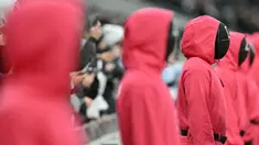 Orang-orang berpakaian seperti penjaga Squid Games dengan berdiri di area penonton selama pertandingan lanjutan Liga Inggris 2024/2025 antara Tottenham Hotspur melawan Liverpool di Stadion Tottenham Hotspur, London, Inggris Minggu (22/12/2024). Seperti diketahui, aksi tersebut ternyata merupakan promo musim kedua serial Korea Selatan tersebut. (AFP/Glyn Kirk)