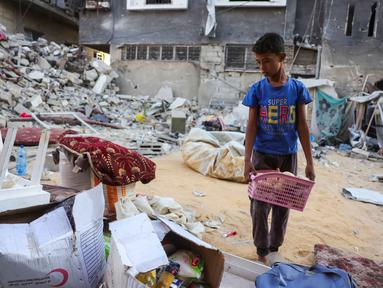 Seorang anak laki-laki menyelamatkan barang-barang dari reruntuhan rumahnya yang hancur akibat serangan Israel di Khan Younis, Jalur Gaza selatan, pada Rabu 29 Oktober 2025. Badan pertahanan sipil Gaza mengatakan pada Rabu 29 Oktober 2025 bahwa puluhan serangan Israel menghantam sejumlah wilayah. (BASHAR TALEB/AFP)