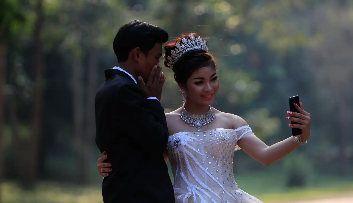 Sepasang pengantin baru berswafoto saat disela pengambilan foto pernikahan mereka di kompleks kuil Angkor Wat, sebuah candi ikonik dan bersejarah di Kamboja, 14 Maret 2018. Arti nama dari Angkor Wat adalah Kota Kuil. (AP Photo/Heng Sinith)