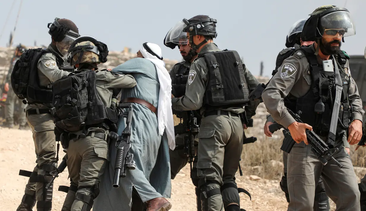 Pasukan penjaga perbatasan Israel menahan seorang pria Palestina di tengah-tengah bentrokan dengan para pengunjuk rasa yang berdemonstrasi menentang pembangunan pos terdepan Israel di dekat desa Palestina, Ramallah, Tepi Barat, Kamis (17/10/2019). (Jaafar ASHTIYEH/AFP)