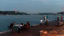 Orang-orang menikmati malam di sebelah pantai Bosphorus ketika jembatan Fatih Sultan Mehmet terlihat di Istanbul (6/7/2020). Ketika diselesaikan pada 1988, jembatan tersebut menjadi jembatan gantung terpanjang ke-5 di dunia; sekarang jembatan tersebut berada pada urutan ke-19. (AFP/Ozan Kose)