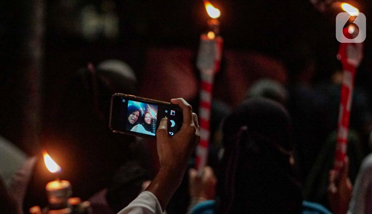 Warga mengambil foto saat mengikuti pawai obor menyambut Ramadan di kawasan Matraman Dalam, Jakarta, Minggu (27/3/2022). Pawai obor tersebut juga digelar untuk meningkatkan silaturahmi dan ukhuwah sesama umat Muslim serta menyemarakkan syiar Islam di Ibu Kota. (Liputan6.com/Faizal Fanani)